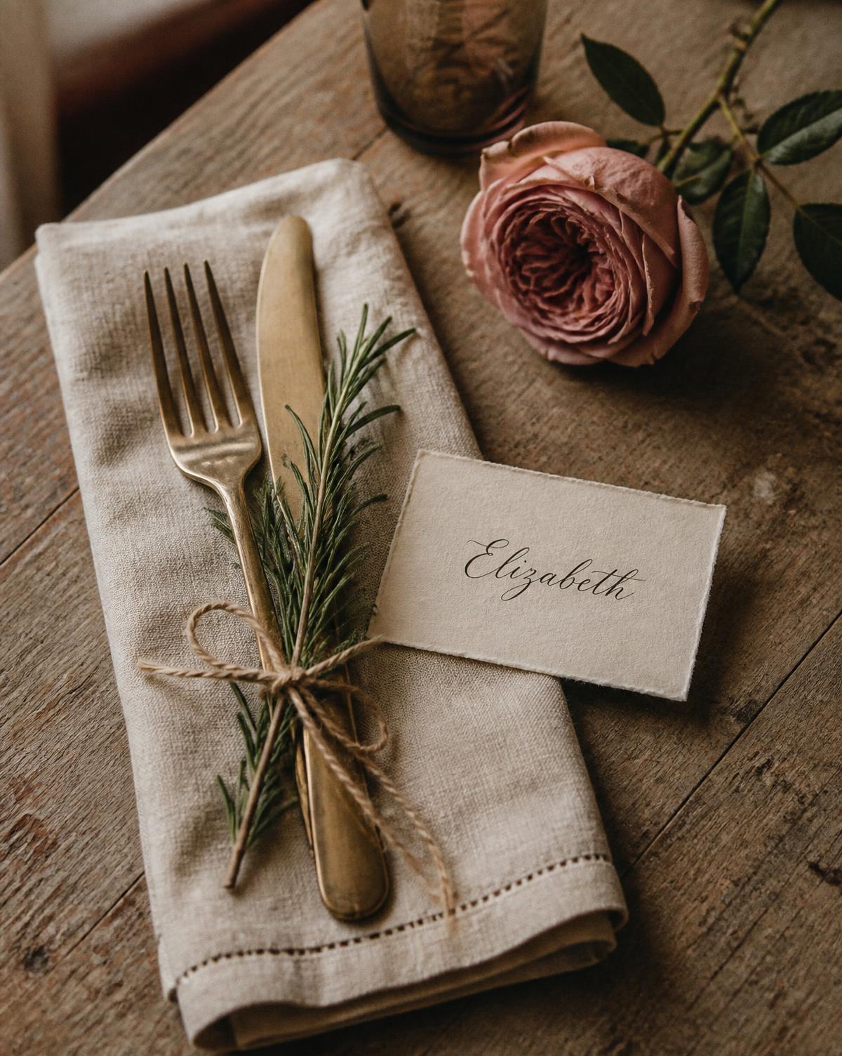 Brass flatware, folded linen and a calligraphed place card on a wooden table