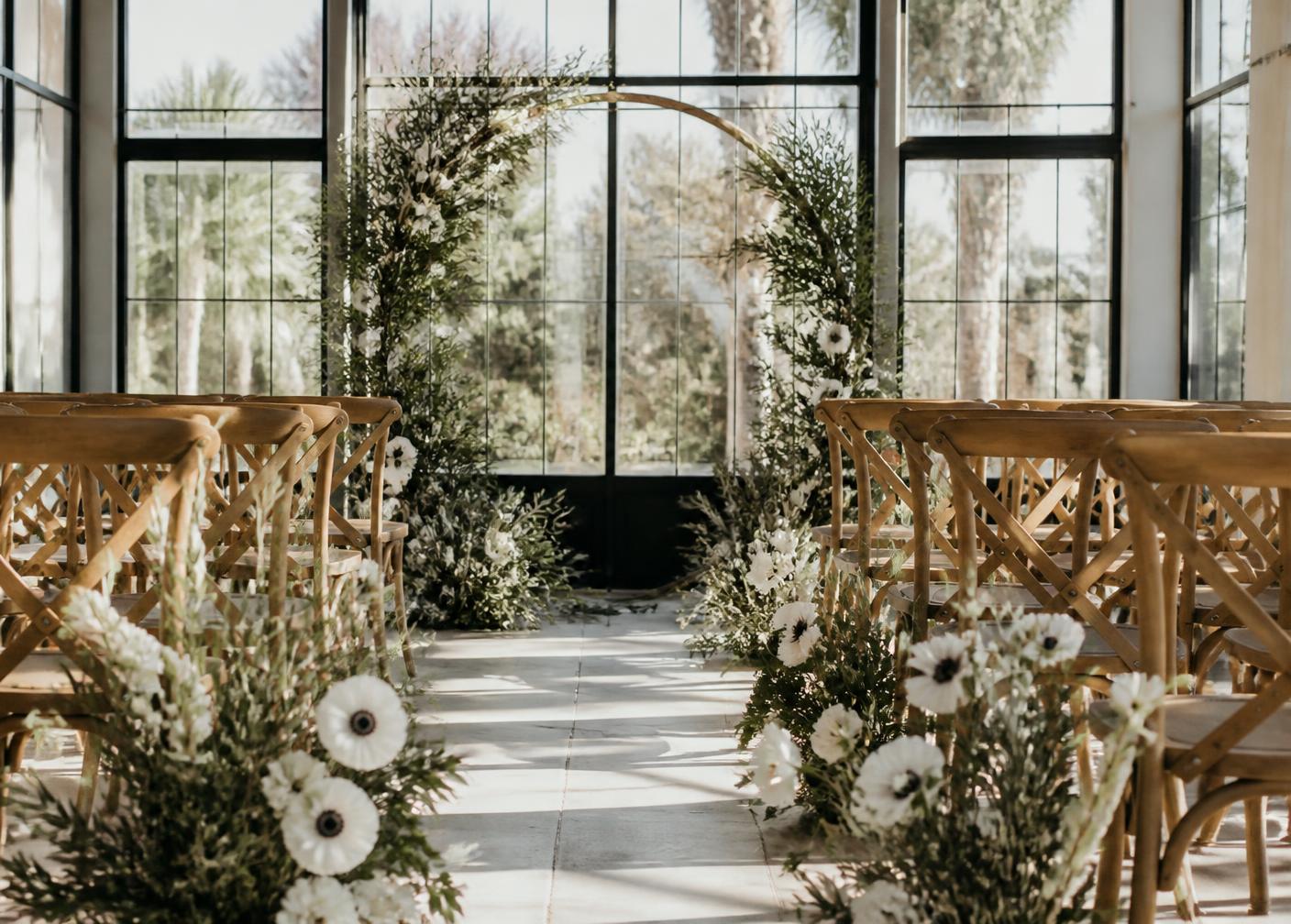 An arch of white anemones and olive branches in the sunlit glass hall